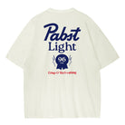An off-white short-sleeve t-shirt showing the back side, which features a large navy blue 'Pabst Light' logo and a red 'Crisp & Refreshing' slogan printed on the back.